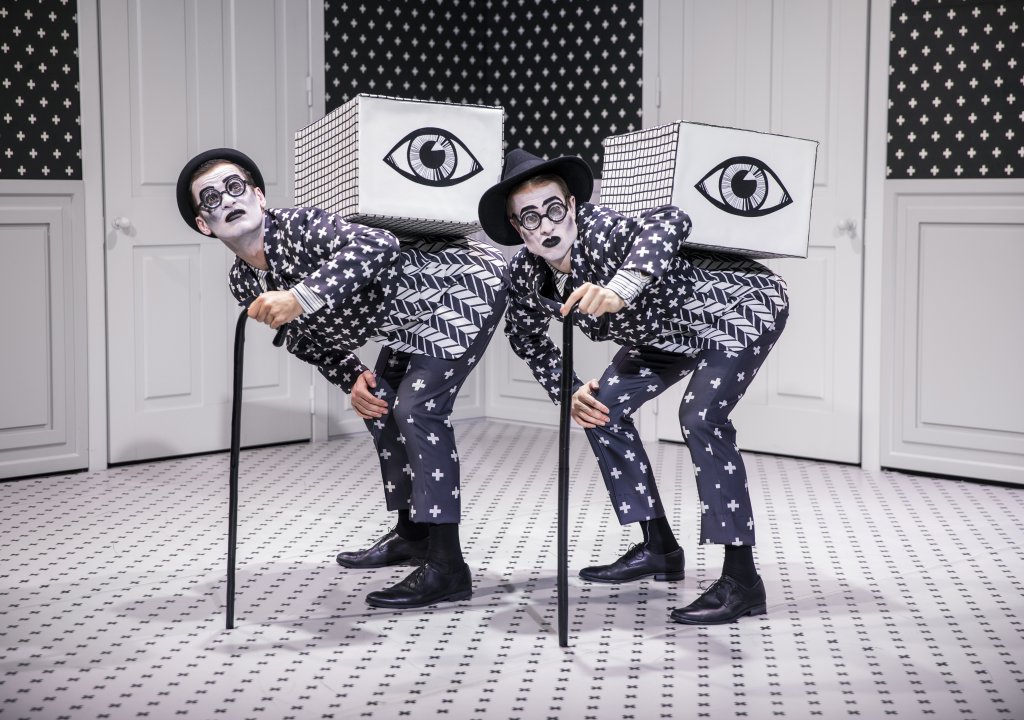 Two dancers with walking canes and boxes with giant eyes on their backs